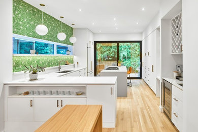 Design ideas for a large scandinavian l-shaped separate kitchen in Toronto with a double-bowl sink, flat-panel cabinets, white cabinets, solid surface benchtops, green splashback, panelled appliances, light hardwood floors, with island, brown floor and white benchtop.