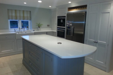 This is an example of a mid-sized contemporary l-shaped eat-in kitchen in Cheshire with a farmhouse sink, shaker cabinets, grey cabinets, quartz benchtops, white splashback, stainless steel appliances, limestone floors and with island.