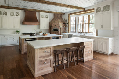 Design ideas for an expansive country kitchen in New York with a farmhouse sink, beaded inset cabinets, light wood cabinets, quartz benchtops, white splashback, engineered quartz splashback, stainless steel appliances, medium hardwood floors, multiple islands, brown floor, white benchtop and timber.