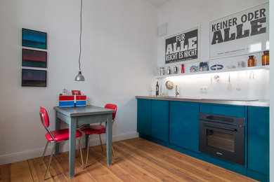 Einzeilige, Kleine Industrial Küche ohne Insel mit flächenbündigen Schrankfronten, blauen Schränken, Edelstahl-Arbeitsplatte, Küchenrückwand in Weiß, schwarzen Elektrogeräten, braunem Holzboden und braunem Boden in Berlin