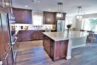 Design ideas for a large transitional l-shaped eat-in kitchen in Houston with an undermount sink, shaker cabinets, medium wood cabinets, granite benchtops, multi-coloured splashback, mosaic tile splashback, stainless steel appliances, vinyl floors, with island and brown floor.