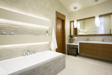 Example of a large trendy master beige tile, gray tile and stone tile ceramic tile drop-in bathtub design in San Diego with flat-panel cabinets, medium tone wood cabinets, beige walls and quartz countertops