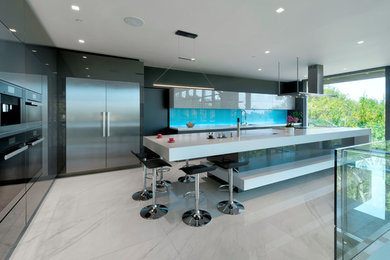 Huge trendy l-shaped porcelain tile and white floor eat-in kitchen photo in Nice with an integrated sink, flat-panel cabinets, gray cabinets, solid surface countertops, blue backsplash, glass tile backsplash, stainless steel appliances, an island and white countertops