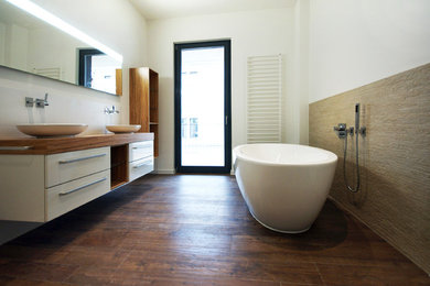 Modernes Badezimmer En Suite mit Aufsatzwaschbecken, flächenbündigen Schrankfronten, weißen Schränken, Waschtisch aus Holz, freistehender Badewanne und weißer Wandfarbe in Leipzig