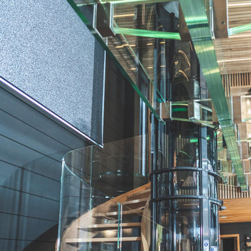 Bogentreppen aus Holz mit Glasgeländer, Fahrstuhl und Glasbrücke - Siller Treppe
