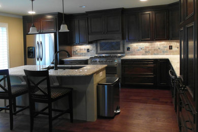 Mid-sized traditional l-shaped eat-in kitchen in DC Metro with an undermount sink, recessed-panel cabinets, dark wood cabinets, granite benchtops, black splashback, stone tile splashback, stainless steel appliances, dark hardwood floors and multiple islands.