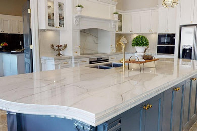 Photo of an expansive classic l-shaped kitchen pantry in Other with a submerged sink, shaker cabinets, quartz worktops, white splashback, marble splashback, stainless steel appliances, porcelain flooring, an island, beige floors and white worktops.