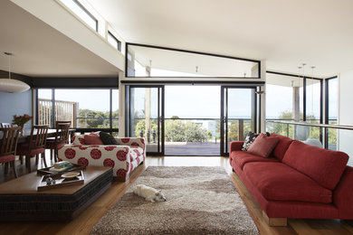 Photo of a large beach style open concept living room in Melbourne with medium hardwood floors, white walls, a two-sided fireplace and a metal fireplace surround.