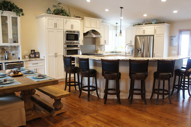 Inspiration for a transitional u-shaped medium tone wood floor open concept kitchen remodel in Minneapolis with a farmhouse sink, shaker cabinets, white cabinets, granite countertops, beige backsplash, cement tile backsplash, stainless steel appliances and an island