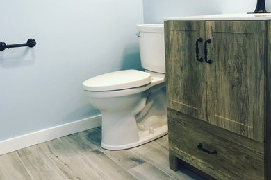 Small country wood-look tile floor, gray floor and single-sink toilet room photo in Boston with recessed-panel cabinets, medium tone wood cabinets, a two-piece toilet, blue walls, quartz countertops, white countertops and a freestanding vanity