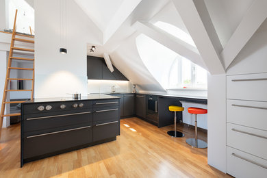 Mittelgroße Moderne Wohnküche ohne Insel mit flächenbündigen Schrankfronten, schwarzen Schränken, Granit-Arbeitsplatte, Küchenrückwand in Weiß, Glasrückwand, schwarzen Elektrogeräten, braunem Holzboden, braunem Boden und schwarzer Arbeitsplatte in München
