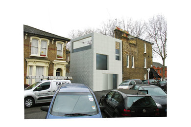 This is an example of a white contemporary brick semi-detached house in London with three floors and a flat roof.