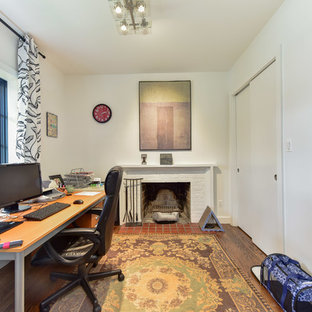 Inspiration for a medium sized modern home office and library with white walls, medium hardwood flooring, a standard fireplace, a brick fireplace surround, a freestanding desk and brown floors.