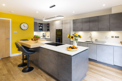 Medium sized modern l-shaped kitchen/diner in Hampshire with a submerged sink, flat-panel cabinets, grey cabinets, quartz worktops, black appliances, medium hardwood flooring, an island, white worktops, all types of ceiling and feature lighting.