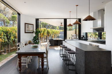 Photo of a contemporary galley open plan kitchen in Sydney with a drop-in sink, white cabinets, solid surface benchtops, mirror splashback, stainless steel appliances, painted wood floors, with island, black floor and grey benchtop.