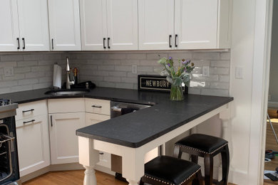 Small transitional l-shaped medium tone wood floor enclosed kitchen photo in Boston with an undermount sink, shaker cabinets, white cabinets, quartz countertops, white backsplash, subway tile backsplash, stainless steel appliances, a peninsula and black countertops