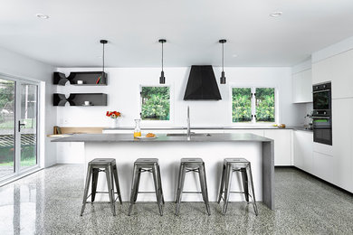 This is an example of a large contemporary l-shaped eat-in kitchen in Other with a double-bowl sink, flat-panel cabinets, white cabinets, quartz benchtops, black appliances, concrete floors, with island and multi-coloured floor.