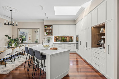 This is an example of a transitional u-shaped kitchen in Perth with an undermount sink, shaker cabinets, white cabinets, panelled appliances, medium hardwood floors, a peninsula, brown floor and white benchtop.