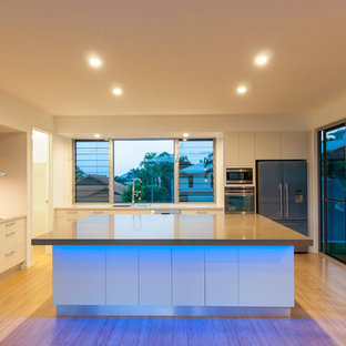 Large beach style kitchen pantry pictures - Kitchen pantry - large beach style l-shaped bamboo floor kitchen pantry idea in Sunshine Coast with an undermount sink, flat-panel cabinets, white cabinets, quartzite countertops, white backsplash, stone tile backsplash, stainless steel appliances and an island