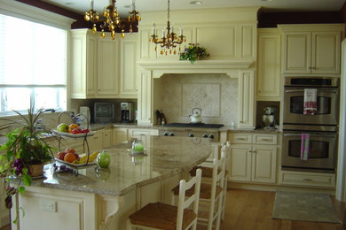 Large elegant l-shaped light wood floor and brown floor eat-in kitchen photo in Montreal with raised-panel cabinets, beige cabinets, granite countertops, beige backsplash, ceramic backsplash, stainless steel appliances and an island