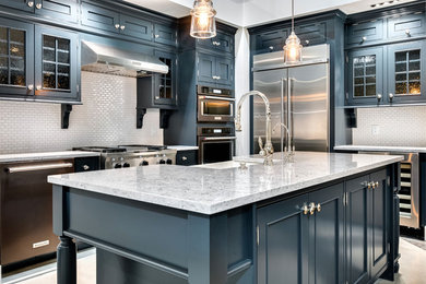 Design ideas for a mid-sized transitional l-shaped separate kitchen in Boise with a farmhouse sink, shaker cabinets, blue cabinets, quartz benchtops, white splashback, subway tile splashback, stainless steel appliances, laminate floors, with island, grey floor and multi-coloured benchtop.