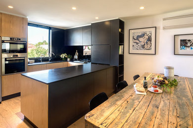 Design ideas for a mid-sized contemporary u-shaped open plan kitchen in Sydney with a double-bowl sink, black splashback, glass sheet splashback, stainless steel appliances, light hardwood floors and black benchtop.