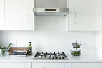 Inspiration for a medium sized contemporary galley kitchen/diner in London with a built-in sink, shaker cabinets, white cabinets, quartz worktops, white splashback, mosaic tiled splashback, stainless steel appliances, vinyl flooring, an island, brown floors and white worktops.