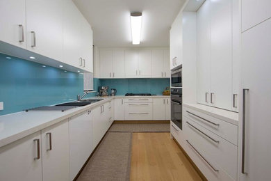 Design ideas for a mid-sized contemporary galley kitchen pantry in Sydney with a drop-in sink, flat-panel cabinets, white cabinets, quartz benchtops, blue splashback, stainless steel appliances, medium hardwood floors, no island and white benchtop.