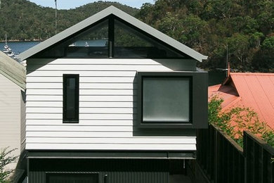 Photo of a small contemporary three-storey white house exterior in Sydney with concrete fiberboard siding, a shed roof and a metal roof.