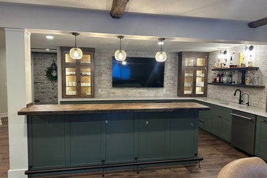 Example of a large mountain style l-shaped vinyl floor and brown floor wet bar design in Detroit with an undermount sink, shaker cabinets, green cabinets, quartzite countertops, gray backsplash, stone tile backsplash and white countertops