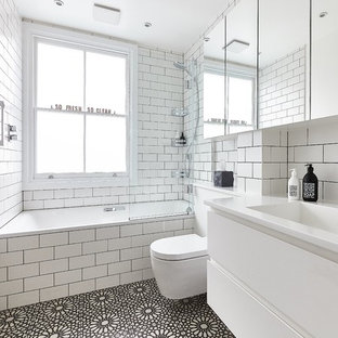 Inspiration for a contemporary shower room in London with flat-panel cabinets, white cabinets, an alcove bath, a shower/bath combination, a wall mounted toilet, white tiles, metro tiles, white walls, cement flooring, an integrated sink, black floors and an open shower.