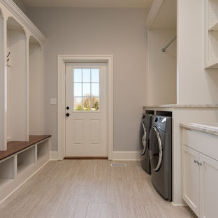 他の地域の大きいトランジショナルスタイルのおしゃれな家事室 (ドロップインシンク、シェーカースタイル扉のキャビネット、白いキャビネット、ライムストーンカウンター、グレーの壁、磁器タイルの床、左右配置の洗濯機・乾燥機、ベージュの床) の写真