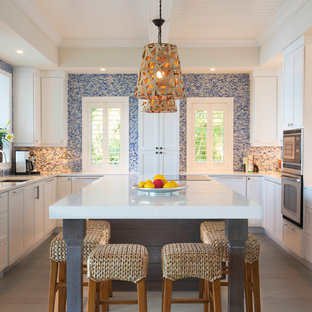 Coastal kitchen remodeling - Example of a beach style u-shaped light wood floor kitchen design in Miami with an undermount sink, shaker cabinets, white cabinets, multicolored backsplash, mosaic tile backsplash, stainless steel appliances, an island and white countertops