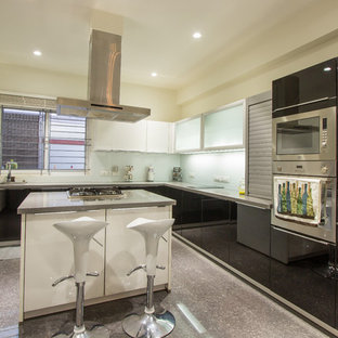 Foto de cocina en L, actual, con armarios con paneles lisos, puertas de armario negras, salpicadero de vidrio templado, electrodomésticos de acero inoxidable y una isla