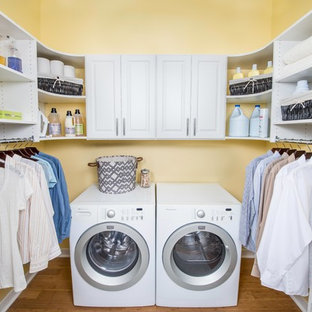 シンシナティの中サイズのおしゃれなランドリールーム (レイズドパネル扉のキャビネット、白いキャビネット、黄色い壁、竹フローリング、左右配置の洗濯機・乾燥機) の写真