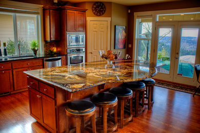 Large traditional l-shaped eat-in kitchen in Seattle with an undermount sink, brown cabinets, granite benchtops, brown splashback, stone tile splashback, stainless steel appliances, recessed-panel cabinets, medium hardwood floors and with island.