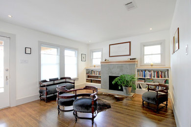 This is an example of a mid-sized transitional enclosed living room in Houston with a library, white walls, medium hardwood floors, a standard fireplace, a concrete fireplace surround, no tv and brown floor.