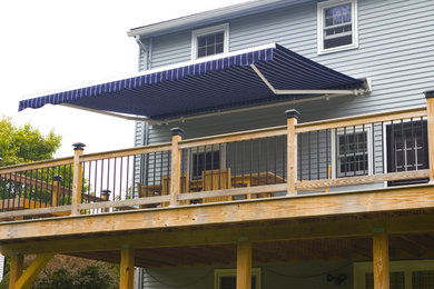 Photo of a mid-sized modern backyard deck in New York with an awning.