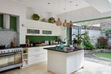 Inspiration for a large contemporary kitchen in London with a built-in sink, shaker cabinets, white cabinets, granite worktops, white splashback, porcelain splashback, limestone flooring, an island, beige floors and black worktops.