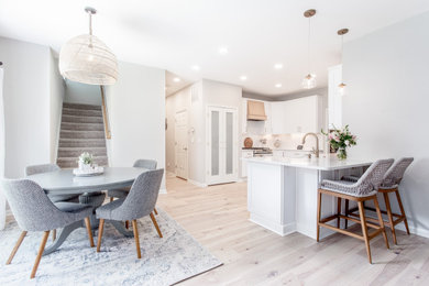 Inspiration for a timeless light wood floor and white floor eat-in kitchen remodel in Atlanta with a farmhouse sink, shaker cabinets, white cabinets, quartz countertops, white backsplash, subway tile backsplash, stainless steel appliances, a peninsula and white countertops