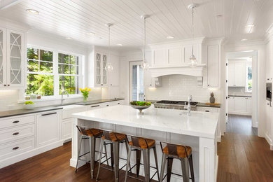 Large transitional u-shaped eat-in kitchen in San Francisco with a farmhouse sink, recessed-panel cabinets, white cabinets, marble benchtops, white splashback, subway tile splashback, panelled appliances, medium hardwood floors, with island, brown floor and white benchtop.