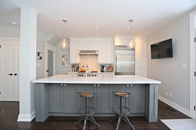 Eat-in kitchen - mid-sized transitional single-wall dark wood floor and brown floor eat-in kitchen idea in Toronto with a farmhouse sink, white cabinets, white backsplash, glass tile backsplash, stainless steel appliances, an island, quartz countertops and shaker cabinets