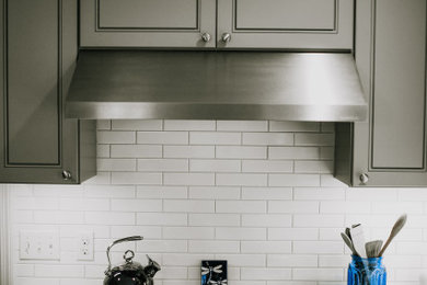 Ejemplo de cocina actual de tamaño medio con armarios estilo shaker, salpicadero blanco, salpicadero de azulejos tipo metro, electrodomésticos de acero inoxidable, una isla y puertas de armario grises