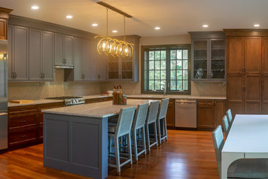 Photo of a large mediterranean l-shaped eat-in kitchen in Philadelphia with a double-bowl sink, raised-panel cabinets, dark wood cabinets, granite benchtops, grey splashback, ceramic splashback, stainless steel appliances, medium hardwood floors, with island, brown floor and grey benchtop.