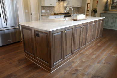 Example of a large single-wall medium tone wood floor open concept kitchen design in Cleveland with an undermount sink, raised-panel cabinets, dark wood cabinets, quartzite countertops, beige backsplash, stone tile backsplash, stainless steel appliances, two islands and white countertops