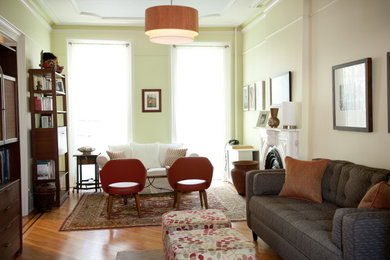 Example of a large eclectic enclosed medium tone wood floor living room design in New York with green walls, a standard fireplace and a plaster fireplace