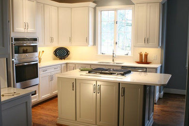 Example of a classic l-shaped dark wood floor kitchen design in Birmingham with a double-bowl sink, recessed-panel cabinets, white cabinets, quartz countertops, white backsplash, stainless steel appliances and an island