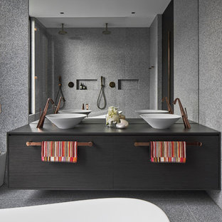 Ispirazione per una stanza da bagno moderna con ante lisce, ante nere, vasca freestanding, piastrelle grigie, lavabo a bacinella, pavimento grigio e top nero