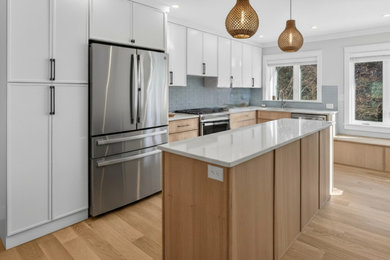 Kitchen - coastal light wood floor kitchen idea in Portland Maine with shaker cabinets, light wood cabinets, quartz countertops, blue backsplash, glass tile backsplash, stainless steel appliances, an island and white countertops