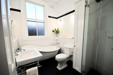 Photo of a traditional master bathroom in Sydney with shaker cabinets, white cabinets, a claw-foot tub, a corner shower, a two-piece toilet, black and white tile, ceramic tile, white walls, ceramic floors, a pedestal sink, solid surface benchtops, black floor, a hinged shower door and white benchtops.